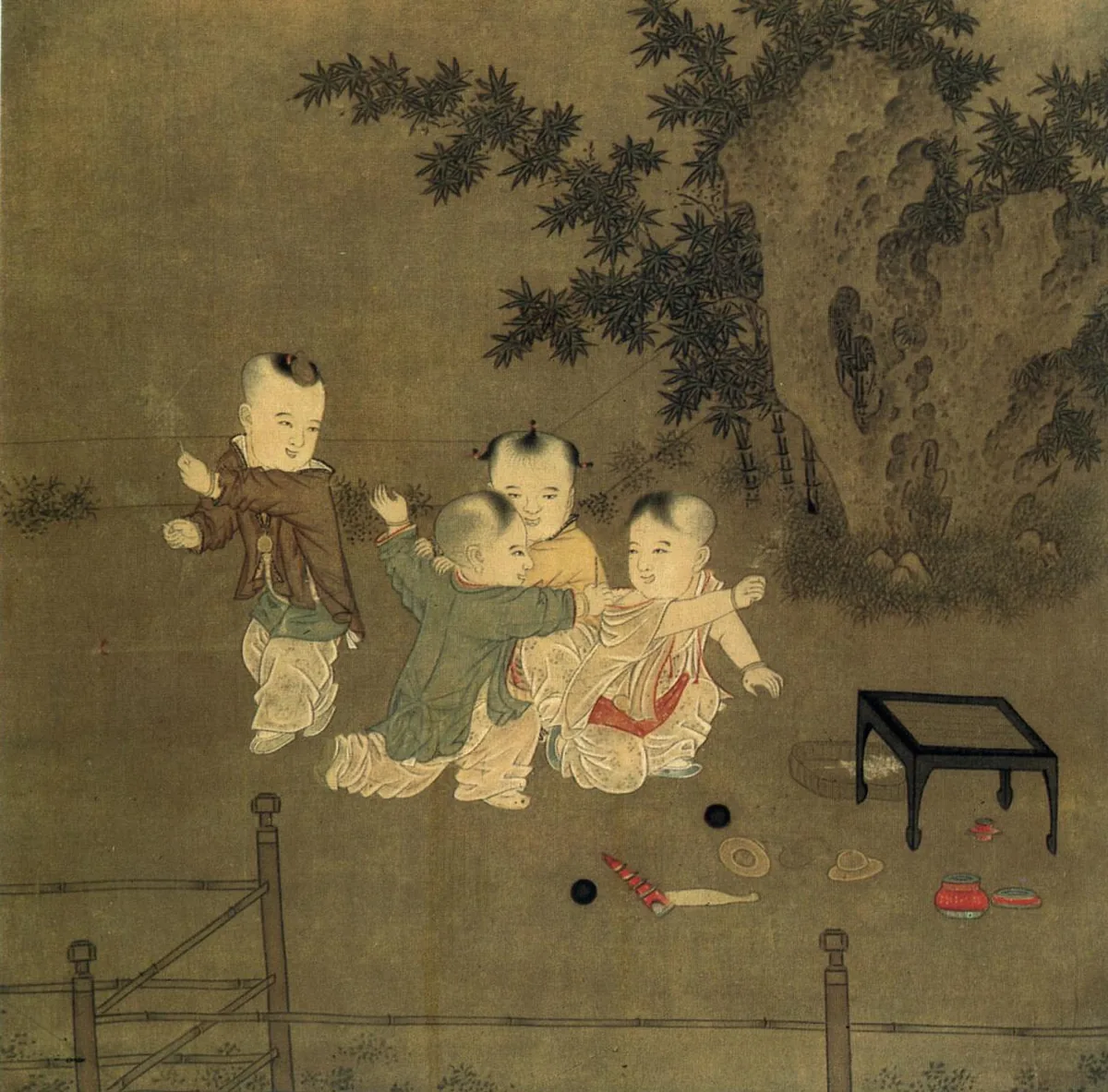 Four young children play together outdoors beside a garden rock and a low fence.